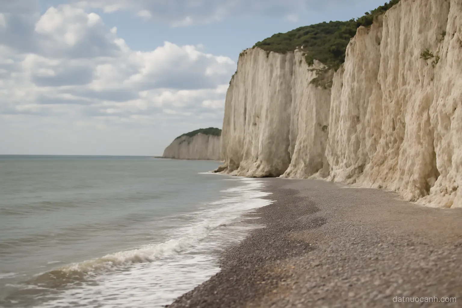 Chalk cliffs meeting a grey sea under scattered cloud, a narrow shingle beach below, no text