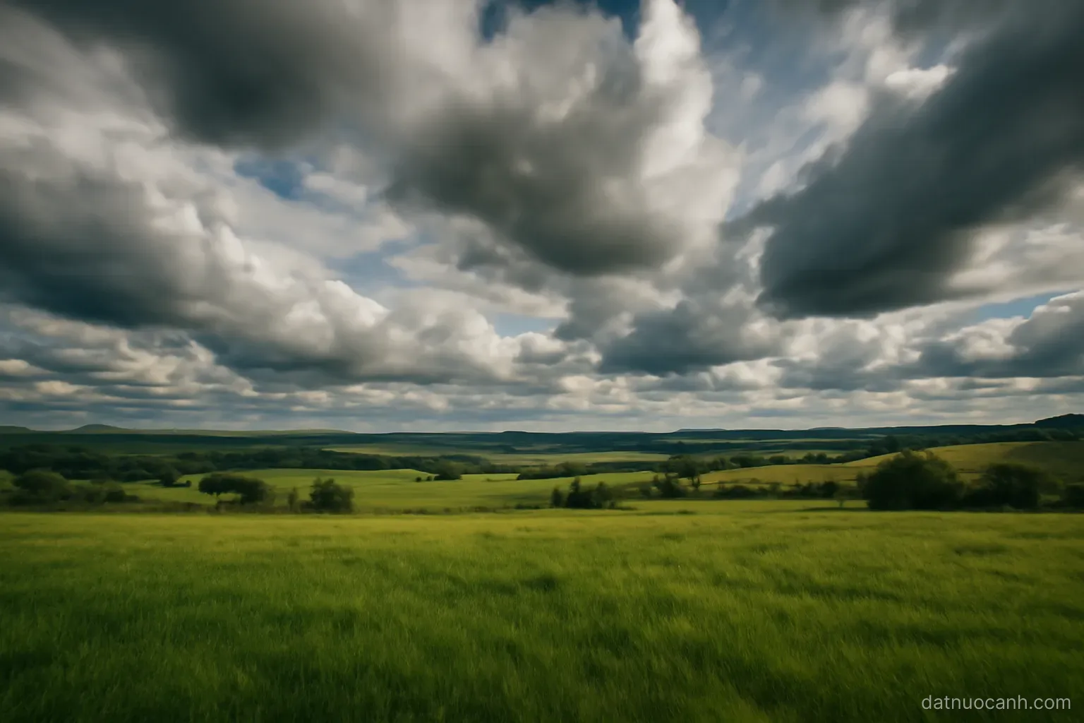 Fast-moving clouds over a green landscape with patches of sunlight and shadow, wide sky, no text